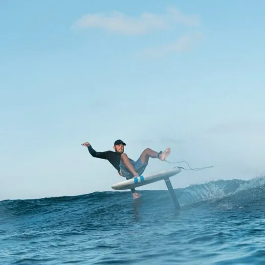 Серфингист выполняет трюк на доске в тёплом океане под ясным небом во время летнего утра