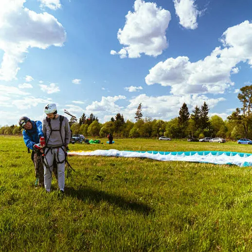 Подготовка к парапланеризму на зелёном поле в солнечный день с облаками