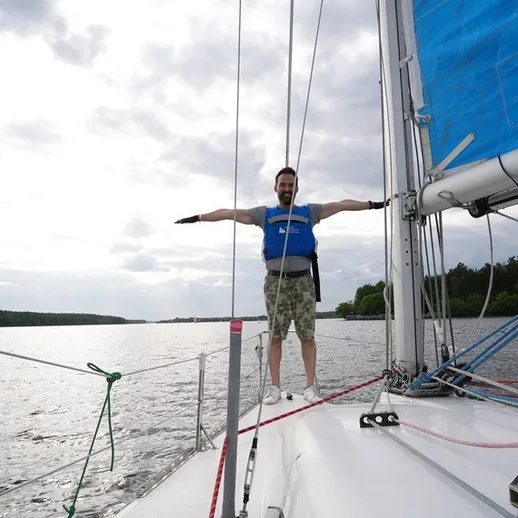 Человек на парусной лодке с расправленными руками на фоне водной глади и облачного неба