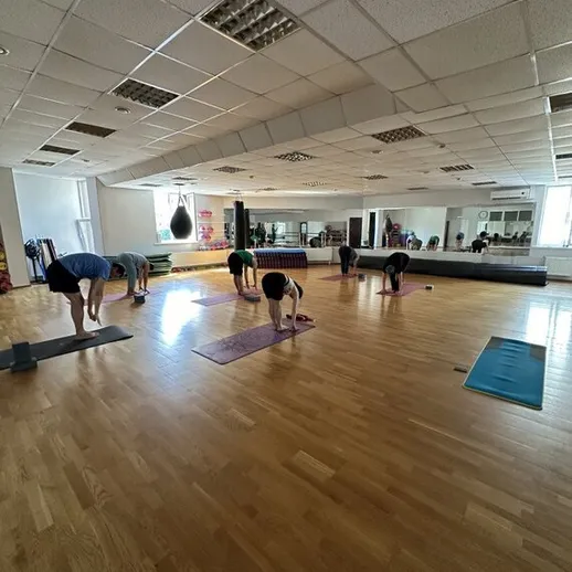 Группа людей выполняет упражнения в зале для занятий фитнесом в утреннее время