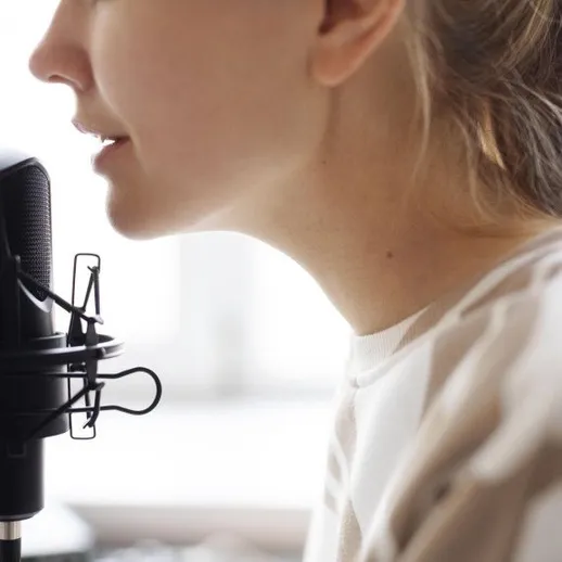 Женщина говорит в микрофон в комнате с окнами и светом, звукозапись проходит