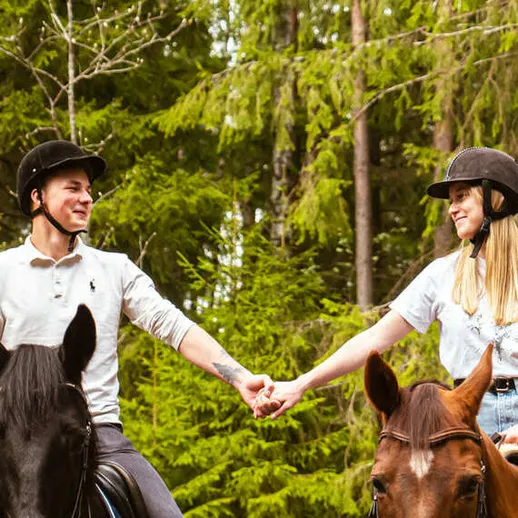Молодая пара держится за руки на лошадях в лесу, наслаждаясь природой и общением в ясный день Молодая пара держится за руки на лошадях в лесу, наслаждаясь природой и общением в ясный день