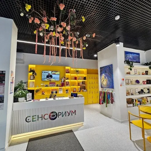 Яркий интерьер сенсорного пространства с желтыми акцентами и цветами на потолке, расположенный в современном городе