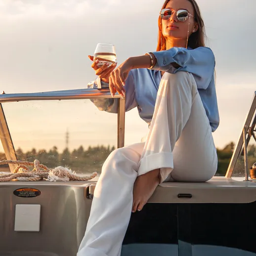 Женщина сидит на борту лодки и держит стакан с напитком в руках в солнечный день