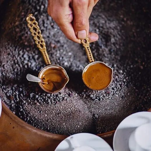 Приготовление кофе на песке в традиционном стиле с использованием медных ложек и чашек в уютной обстановке