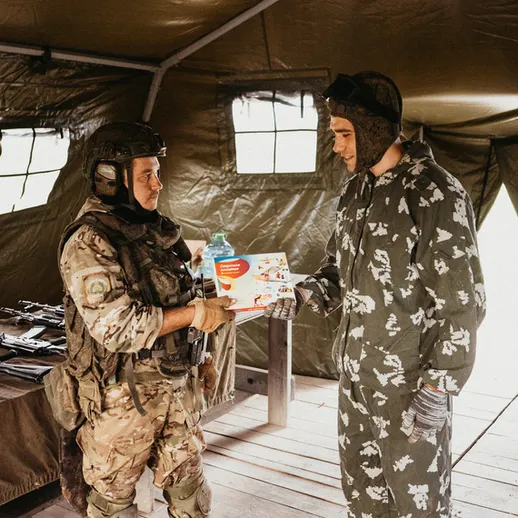Военные учения на базе, солдат передает награду гражданскому лицу в уютном палаточном лагере