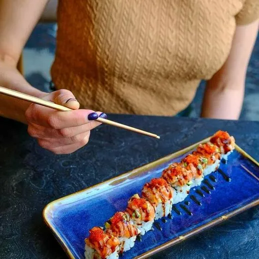 Женщина держит палочки для еды и готовится попробовать суши в уютном ресторане