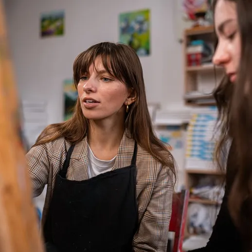 Молодая художница обучает ученицу живописи в творческой мастерской во время урока искусств