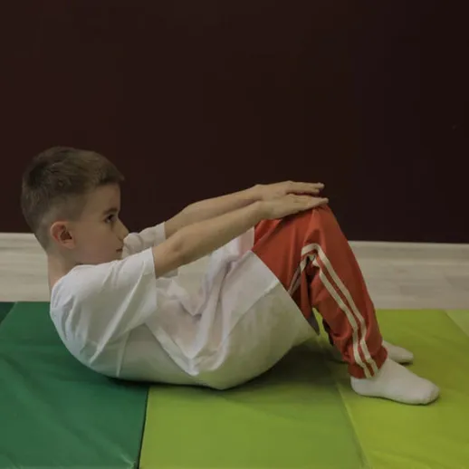 Мальчик выполняет упражнения на коврике в спортзале, сосредоточенный на повышении физической формы и силовой подготовке