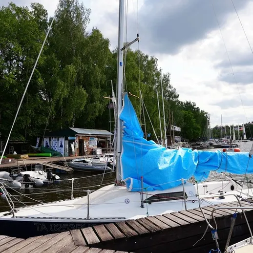 Яхта с синим парусом у причала на реке под облачным небом в летний день