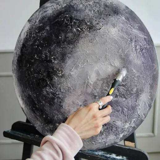 Художник наносит детали на картину луны в уютной студии, окруженной светом и мягкими тонами, утром