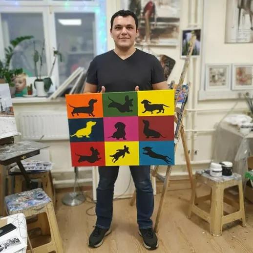 Мужчина держит красочную картину с силуэтами собак в художественной студии