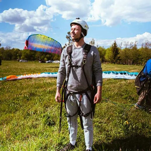 Парапланерист в защитной экипировке готовится к полету на фоне неба и поля