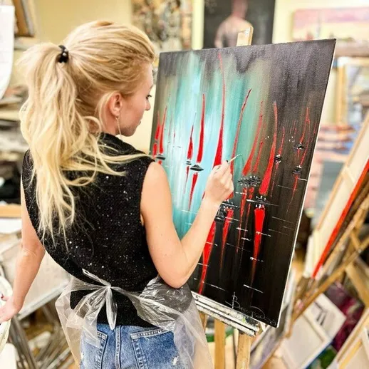 Женщина рисует абстрактную картину с красным и черным на холсте в студии