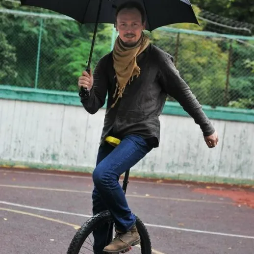 Мужчина катается на одном колесе с зонтом в парке в дождливый день