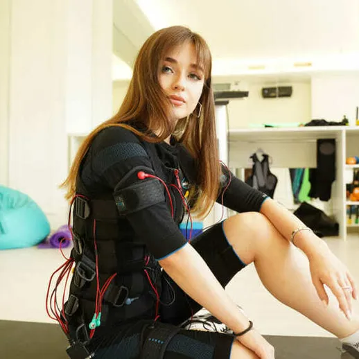 Упражнение с электромиостимуляцией в спортивном зале, молодая женщина в специальном костюме, г. Москва, утро