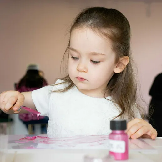 Маленькая девочка рисует яркими красками в студии искусств, сосредоточенно работая над своим проектом в утренние часы