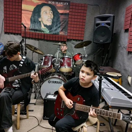 Дети в репетиционном зале играют на гитарах перед барабанщиком в музыкальной атмосфере