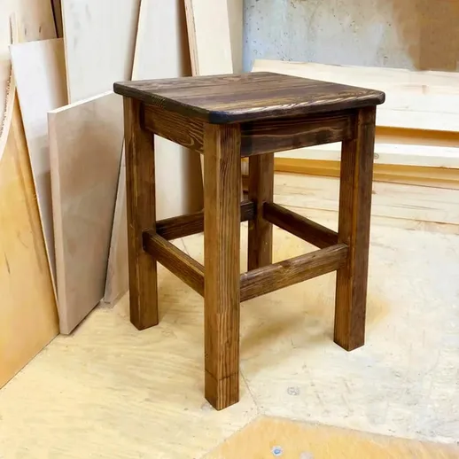 Крафт деревянного табурета в мастерской, окружённой материалами для обработки и строительства