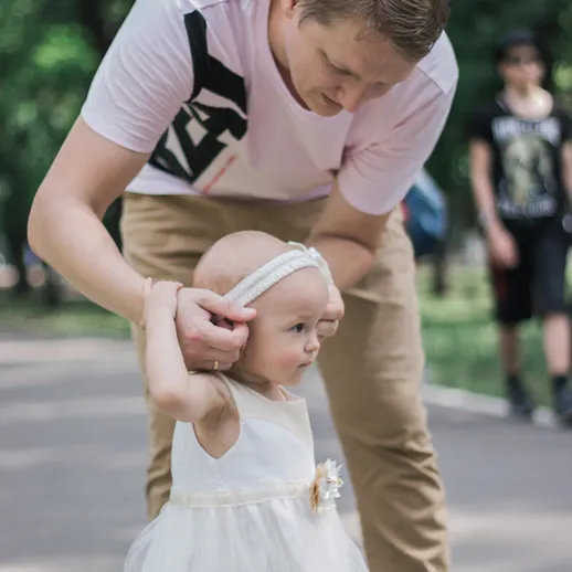 Отец гуляет с дочкой в парке, помогая ей делать первые шаги в солнечный день