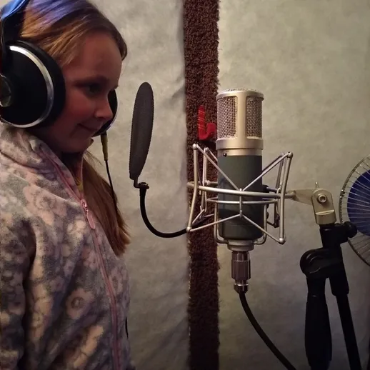 Девочка в наушниках записывает голос в студии звукозаписи в зимней одежде в вечернее время