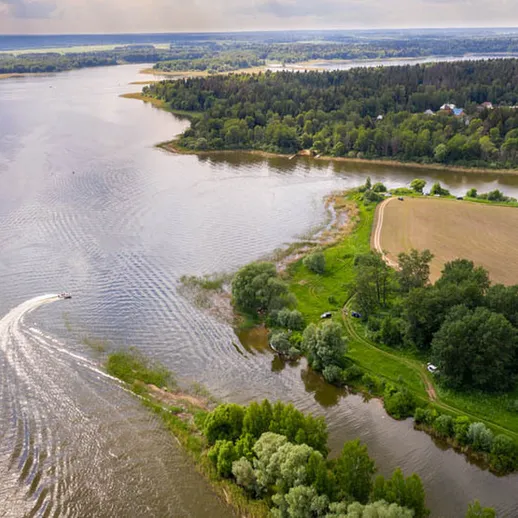 Замечательный вид на реку и её берега с высоты, расположенной недалеко от зеленого леса и полей, в светлое время дня