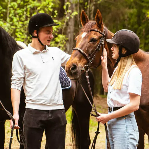 Молодая пара ухаживает за лошадьми на конной прогулке в лесу среди зелёной растительности Молодая пара ухаживает за лошадьми на конной прогулке в лесу среди зелёной растительности