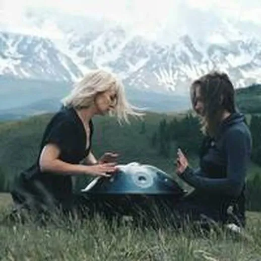 Две музыкантки играют на ханга на фоне горной природы во время ясного дня