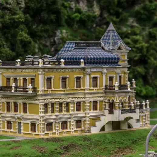 Модель красивого желтого здания с синими крышами на фоне зелёной природы