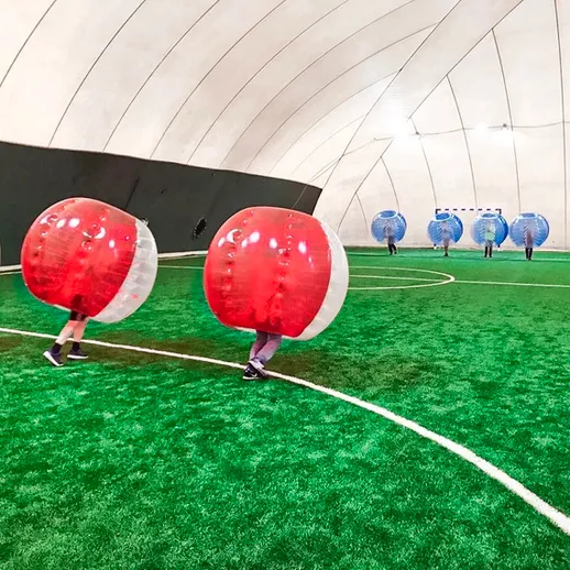 Игроки в пузырях на футбольном поле в крытом спортзале, наслаждаются веселой игрой в бампербол в зимний день