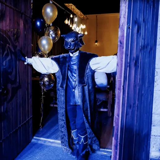 Гостеприимный персонаж в костюме с маской открывает двери на вечеринке в эксклюзивном ресторанном зале