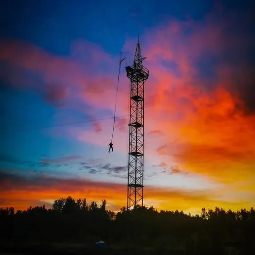 Человек на веревке спускается с вышки на фоне заката в живописном пейзаже