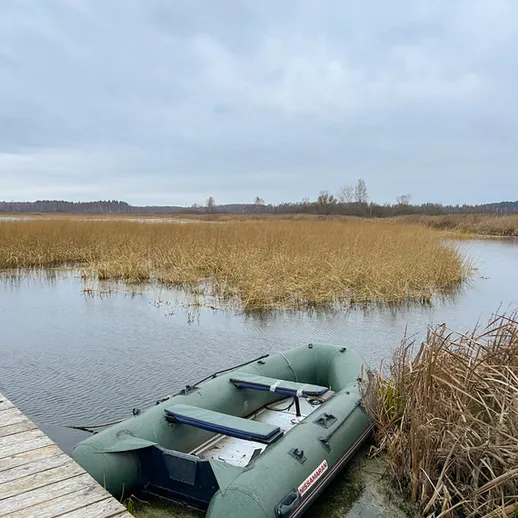 Лодка на берегу реки среди осенних трав под облачным небом