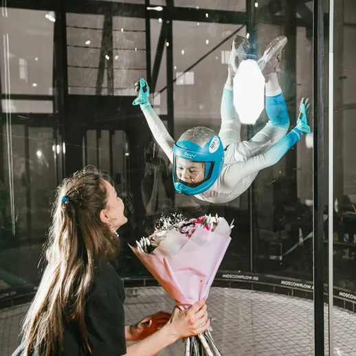 Девочка, летающая в воздухе в аэродинамической трубе, удивляет свою маму с букетом цветов в Москве