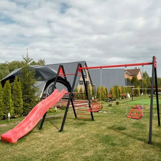 Игровая площадка с горкой и качелями на даче, окруженная зелеными кустами в ясный день