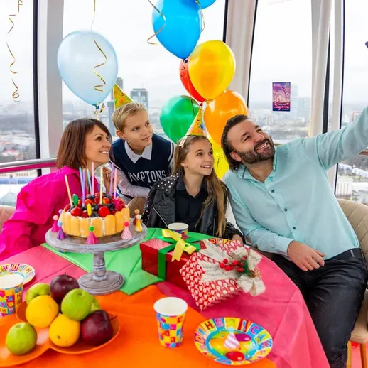 Семейный праздник в кабинке колеса обозрения с тортом, воздушными шарами и радостными улыбками в ясный день