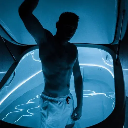 Молодой человек в сенсорной комнате для отдыха с помощью флотирующей ванны и неоновым освещением