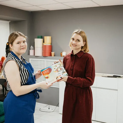 Две женщины обмениваются кулинарной книгой в уютном помещении на мастер-классе по кулинарии в центре города