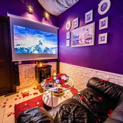 Уютная комната с фиолетовыми стенами и экраном для проекции, украшенная лепестками роз