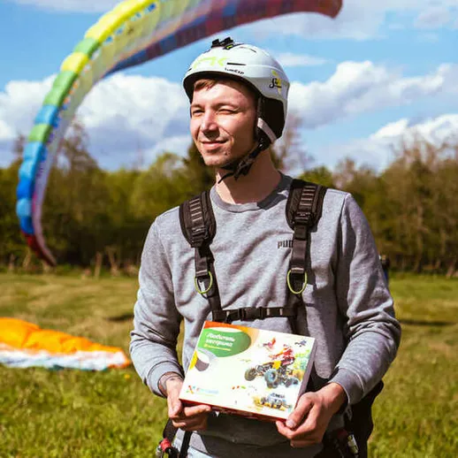 Мужчина с парапланом на фоне зелёного поля и облачного неба держит в руках игрушку в конце летнего дня