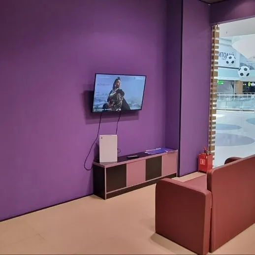 Уютный уголок в торговом центре с телевизором и креслом, заполненный мягким светом и фиолетовыми стенами