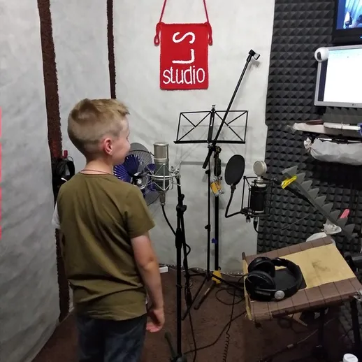 Мальчик записывает голос в звукозаписывающей студии с микрофонами и аппаратурой