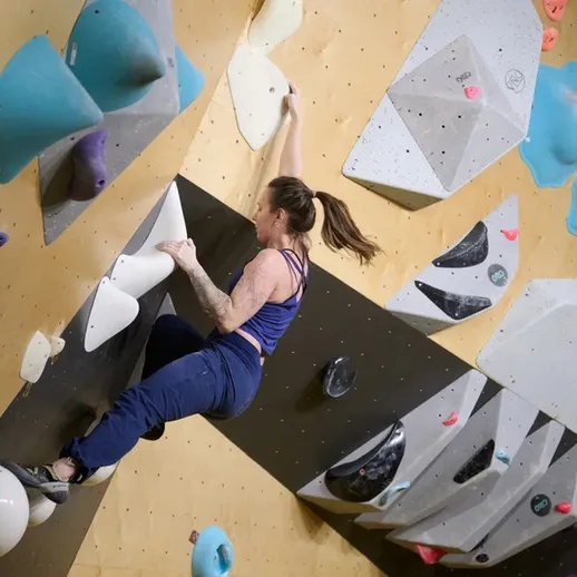 Спортсменка выполняет сложные элементы на скалодроме в закрытом помещении в солнечный день