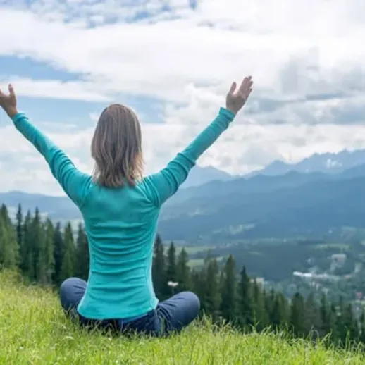 Женщина практикует медитацию на зеленом склоне с видом на горы и облачное небо в летний день