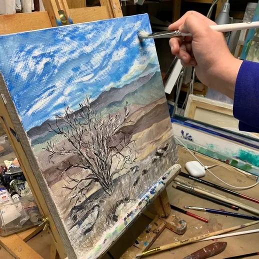 Художник рисует пейзаж с деревом на мольберте в творческой мастерской