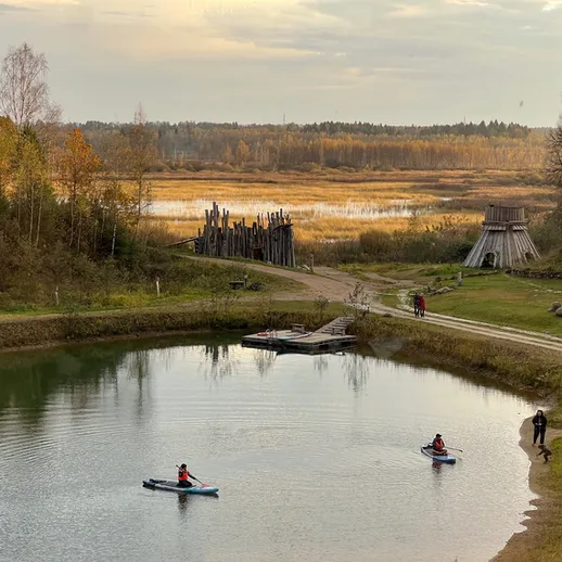 Два человека на каяках наслаждаются спокойствием реки в осенний день, окружённой природой и историческими постройками