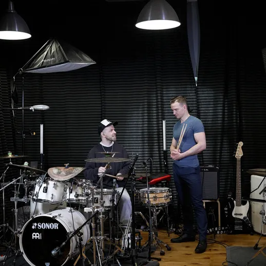 В студии два музыканта репетируют: барабанщик и гитарист готовятся к записи в вечернее время