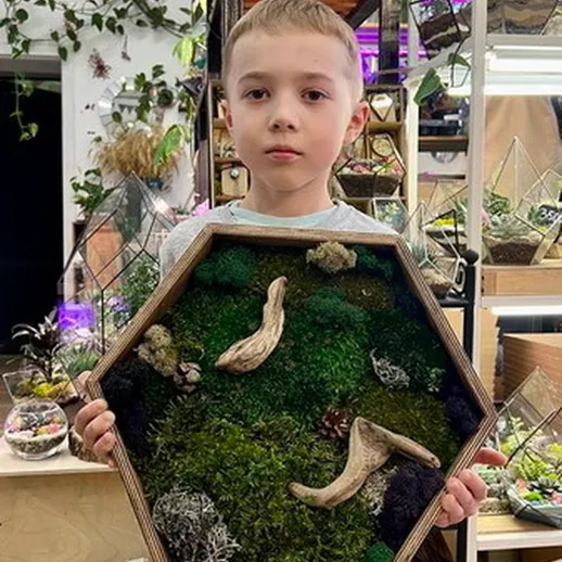 Мальчик показывает уникальную декоративную композицию из мха и древесины в цветочном магазине
