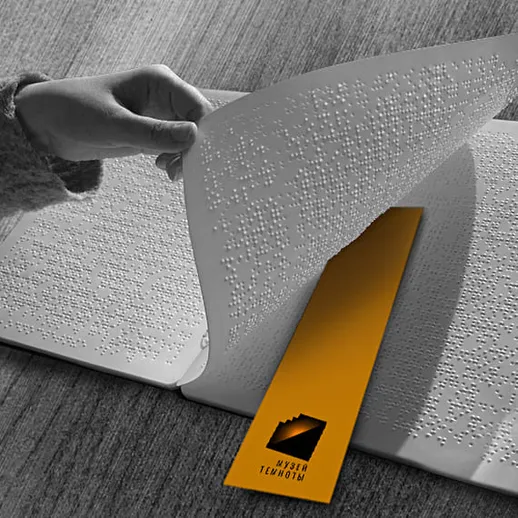 Человек читает книгу с тактильным текстом на Брайлевском шрифте в офисе