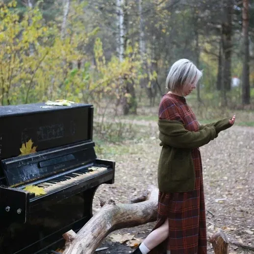 Девушка с короткими волосами играет на старом рояле в лесу среди осенних листьев